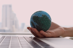"Person holding a model of a globe on top of a laptop."